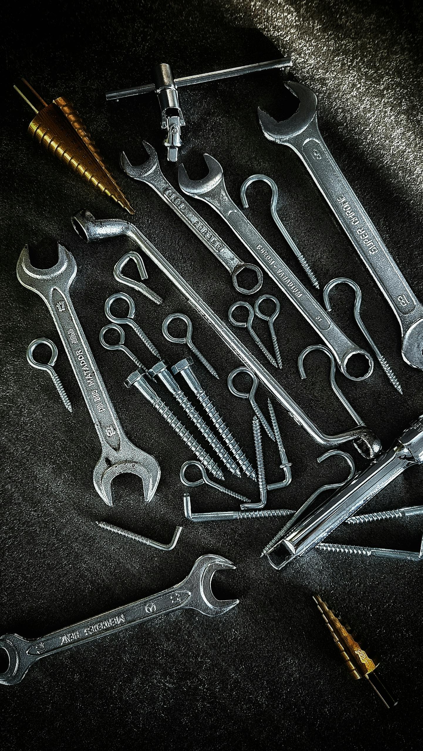 A collection of metal tools including wrenches and screws arranged on a dark background.