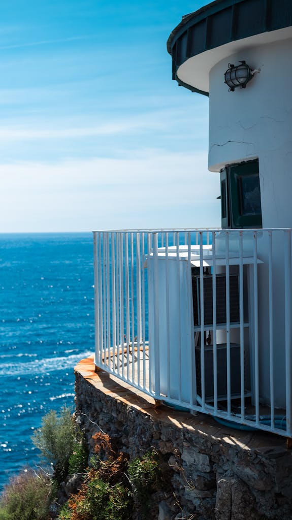 A picturesque lighthouse perched on a cliff in Liguria, Italy, overlooking the vibrant blue sea.