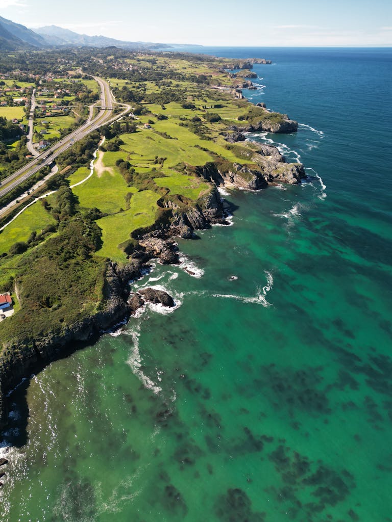 A stunning aerial view of the rugged coastline near Escamplero, Spain, showcasing lush greenery and vibrant blue waters.